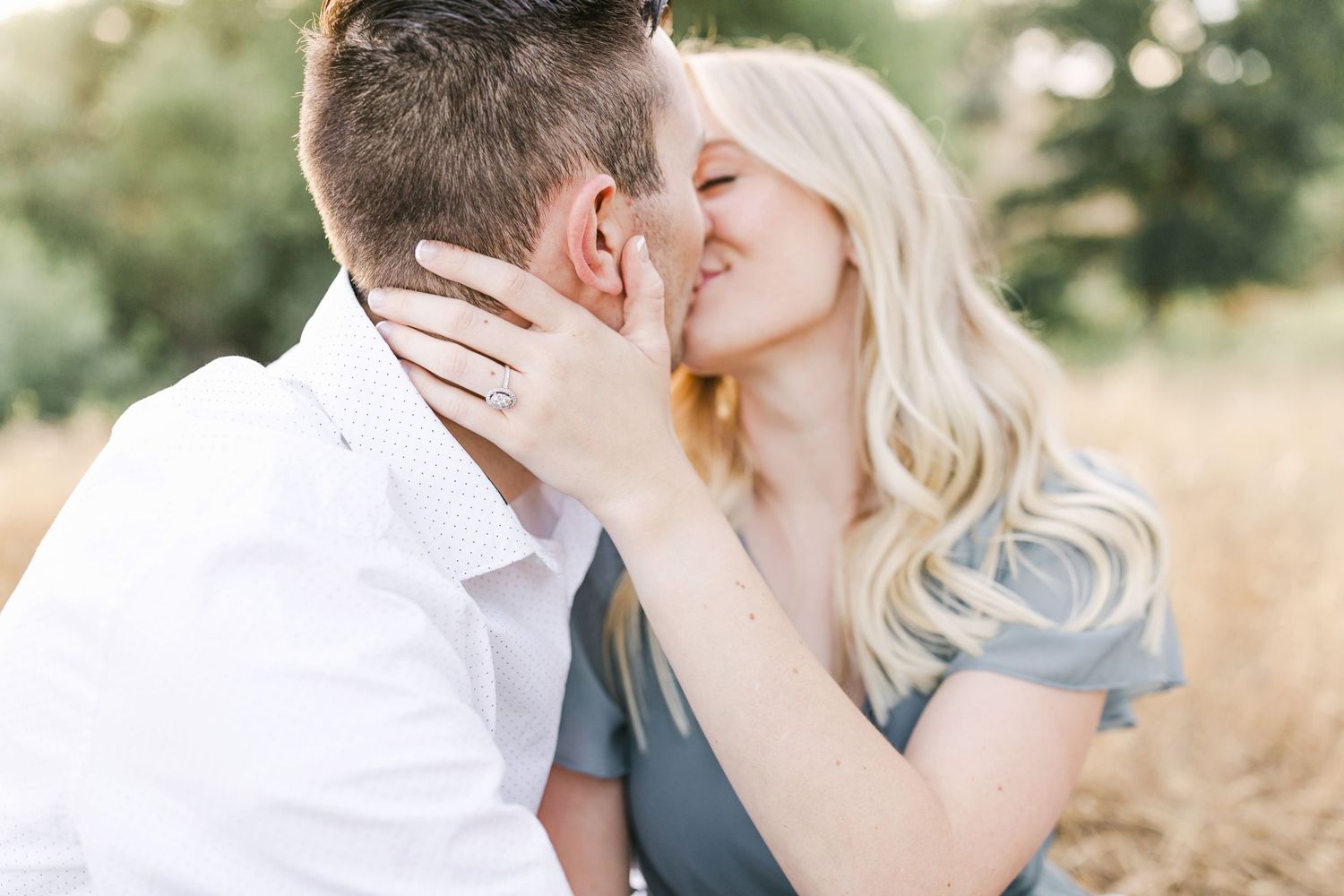 A romantic couple sharing a tender kiss in a sunlit field with golden wheat stalks in the background.