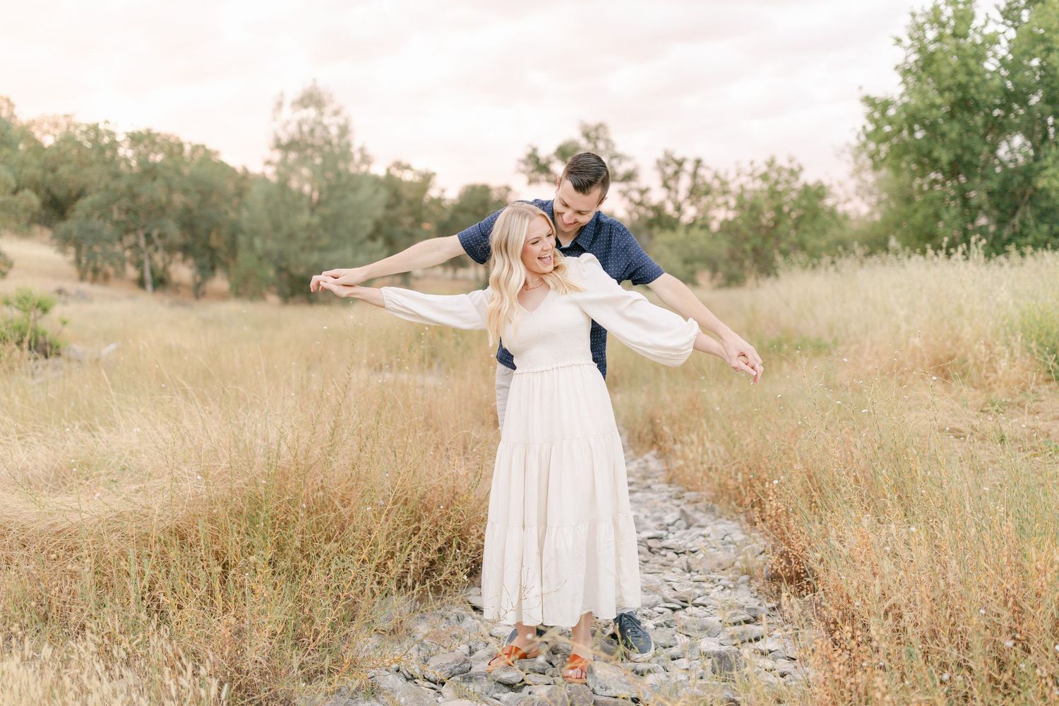 Woman in white dress spins joyfully in field during golden hour.