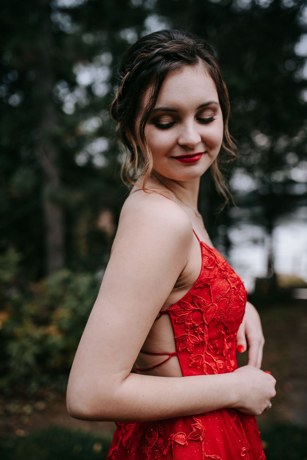 A woman in a red lace dress poses against a dark outdoor background with her eyes closed.
