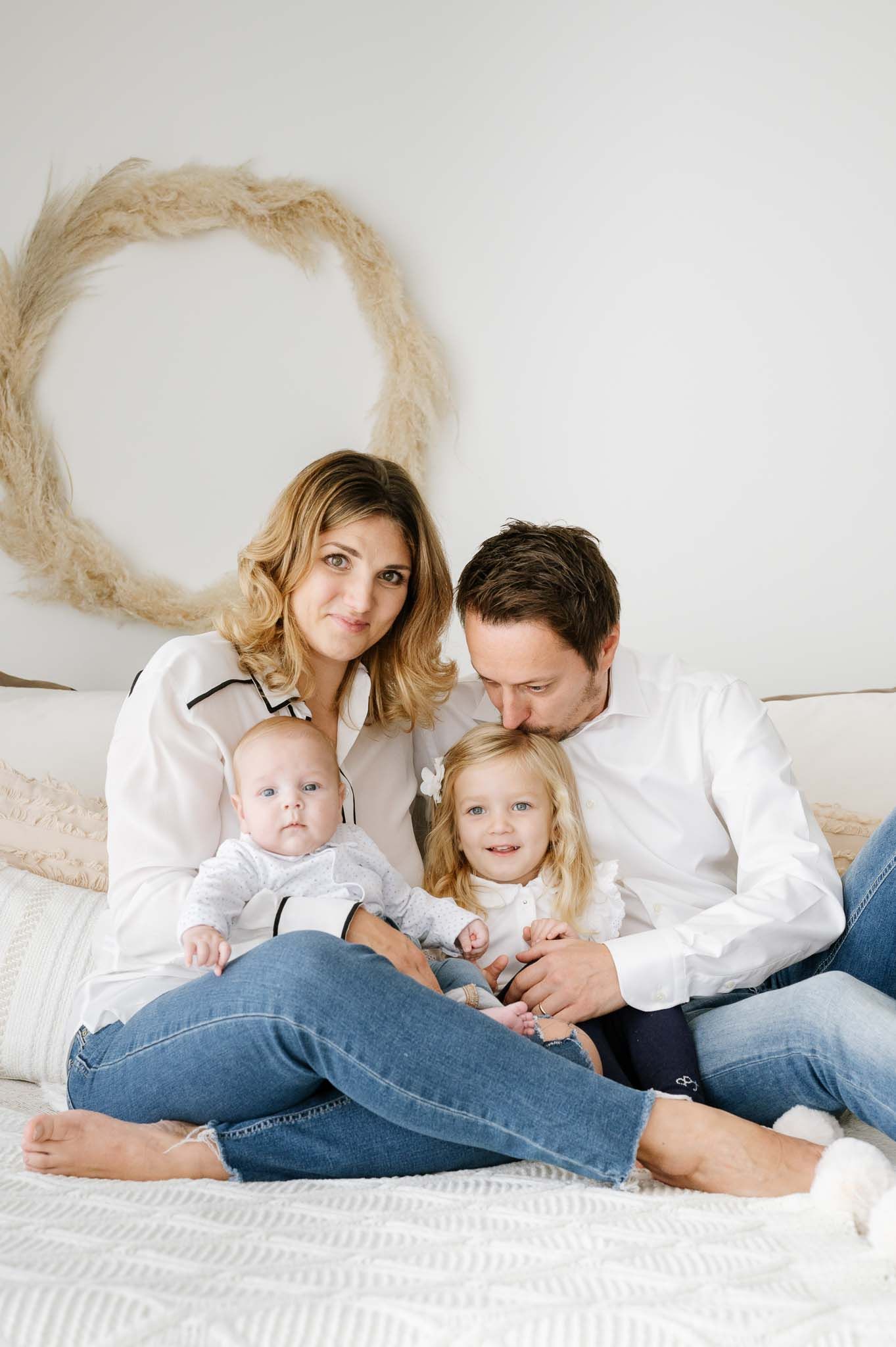 Family portrait on bed with two children and decorative wreath on wall.