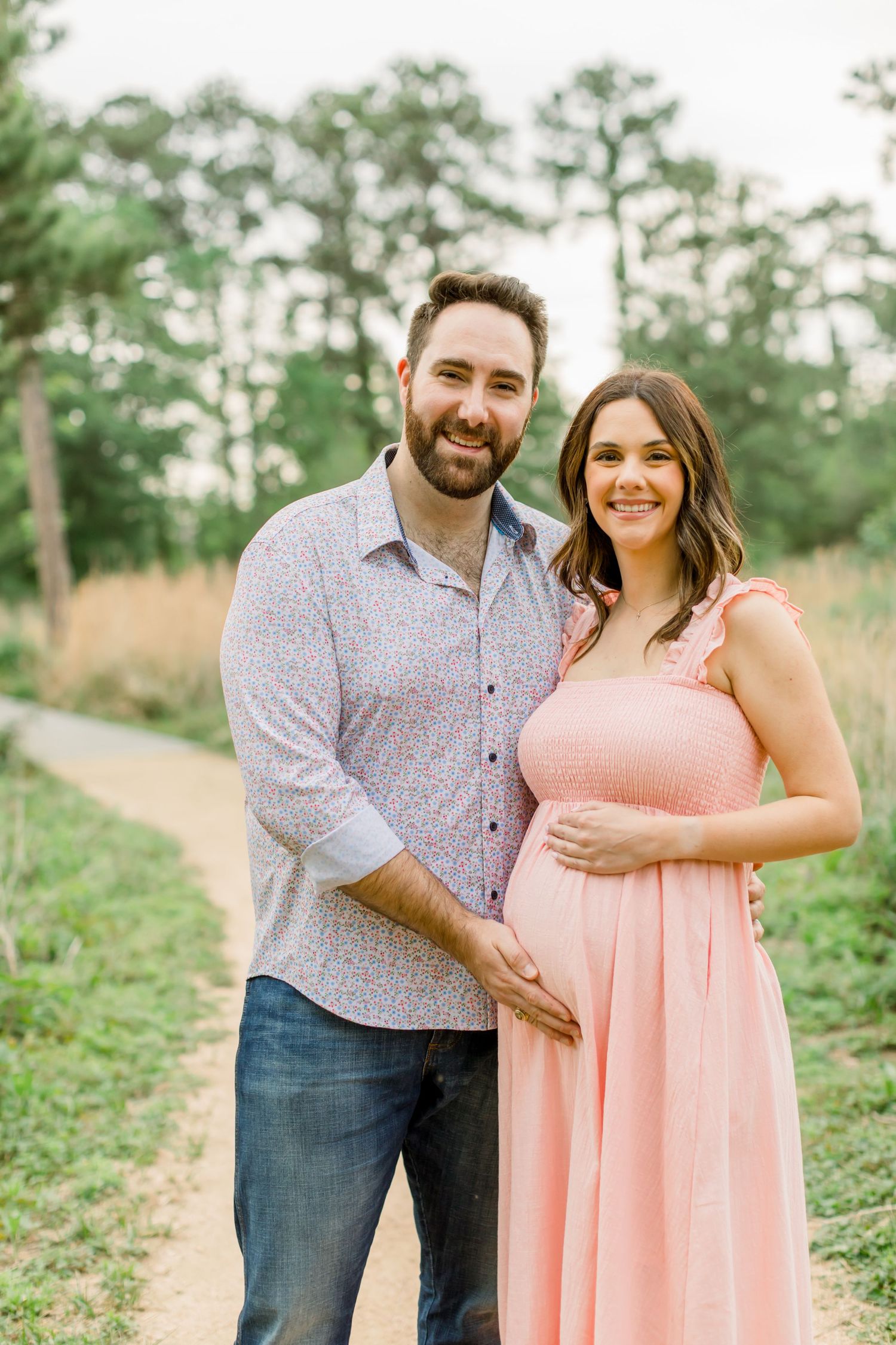 A cheerful couple poses on a nature path wearing coordinated casual outfits against a green forest backdrop.
