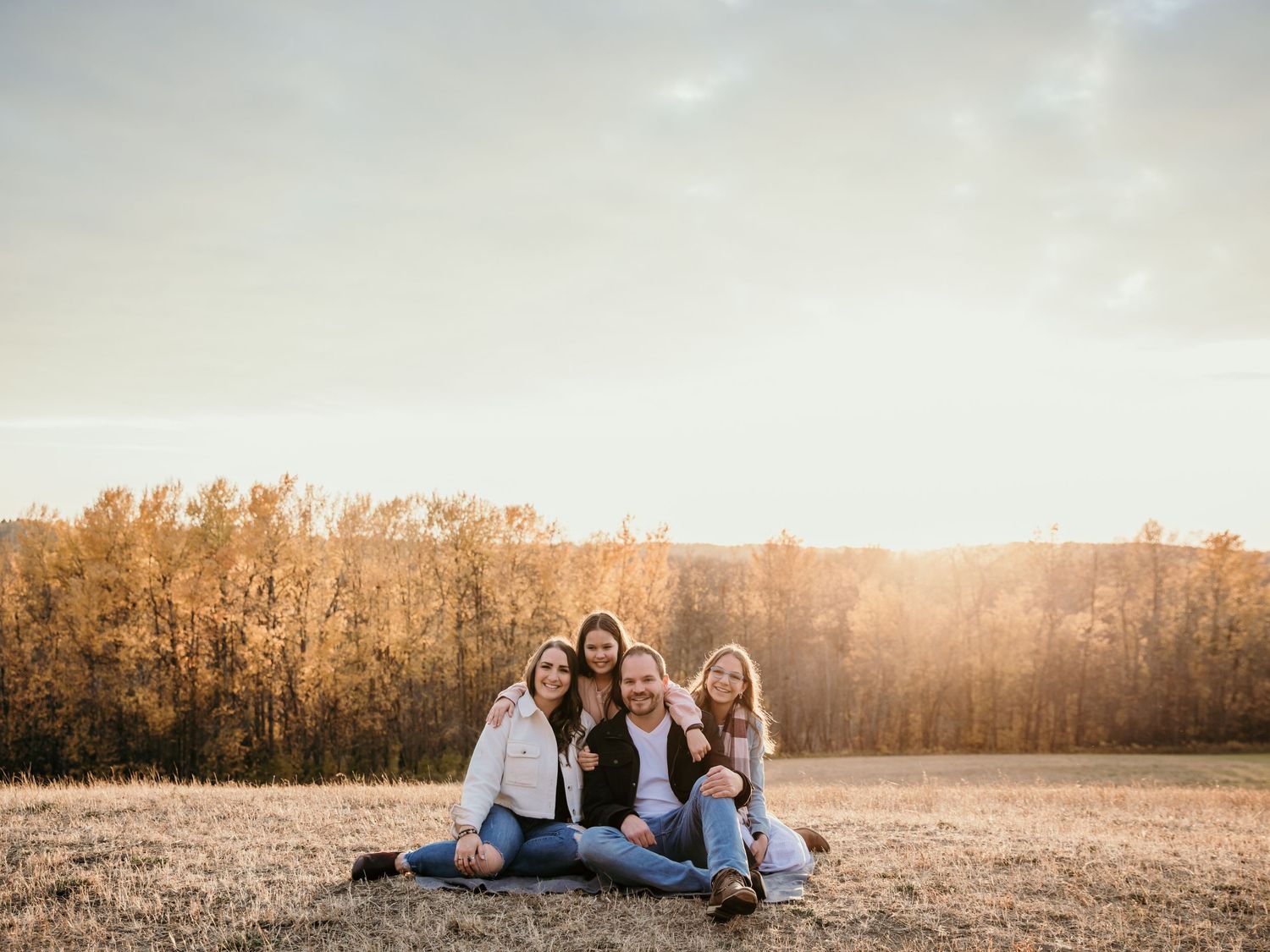Group sitting together in a sunlit field during golden hour with autumn trees in background.