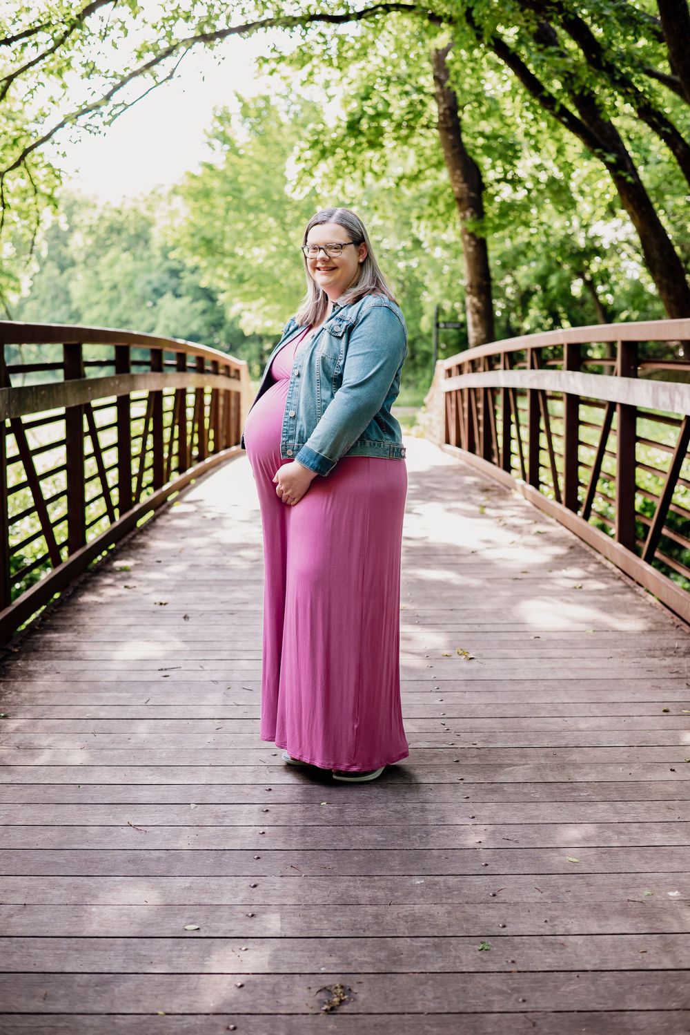 Maternity photos on wooden bridge with lush green trees in background.