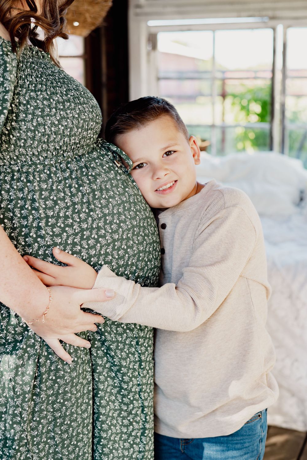Maternity photo with green floral dress and cream sweater in rustic setting.