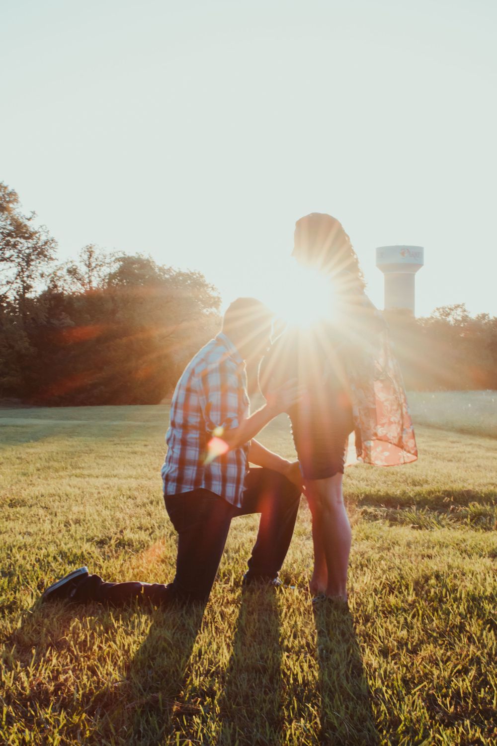 Couple silhouetted against golden sunset in grassy field wearing plaid and casual attire.