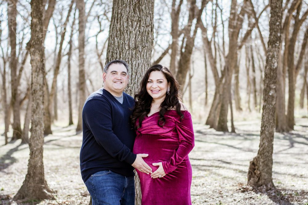 Couple posing together in winter woods setting with woman in velvet burgundy dress.