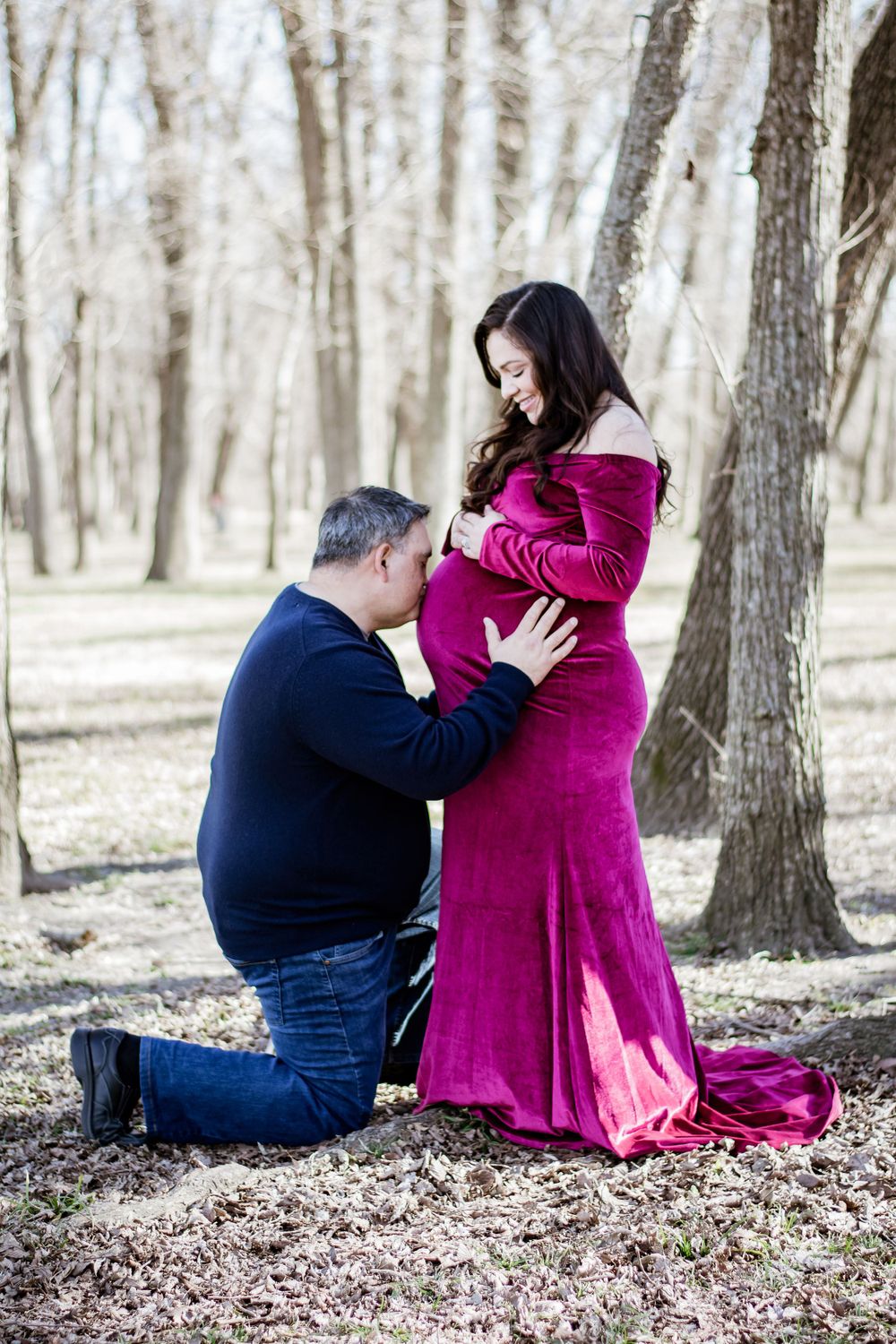 Maternity photo of couple in winter woods with burgundy dress.