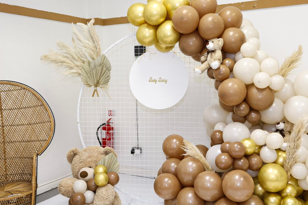 Elegant balloon arch in gold and neutral tones decorates a modern event space with peacock chair.