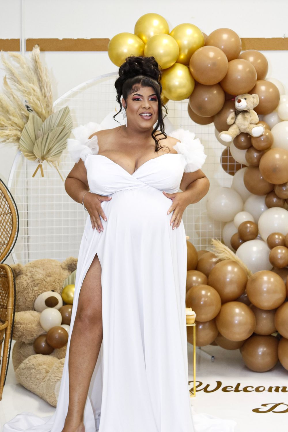 Maternity photo featuring a white dress with thigh slit and gold balloon arch decorations.