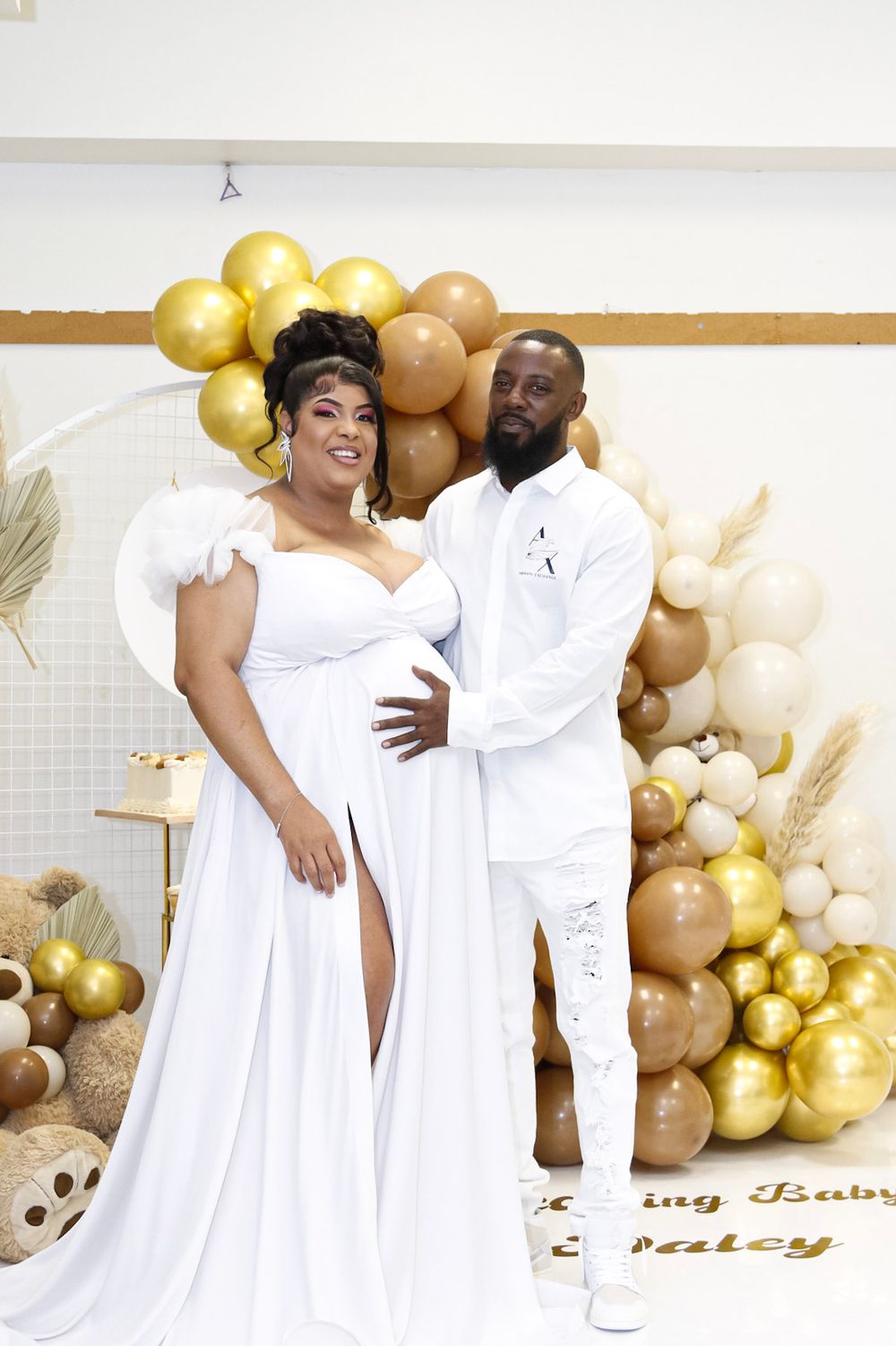 A couple poses together against a backdrop of gold and neutral colored balloons.