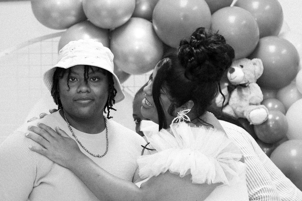Black and white photo of guests at a baby shower celebration with balloon decorations.