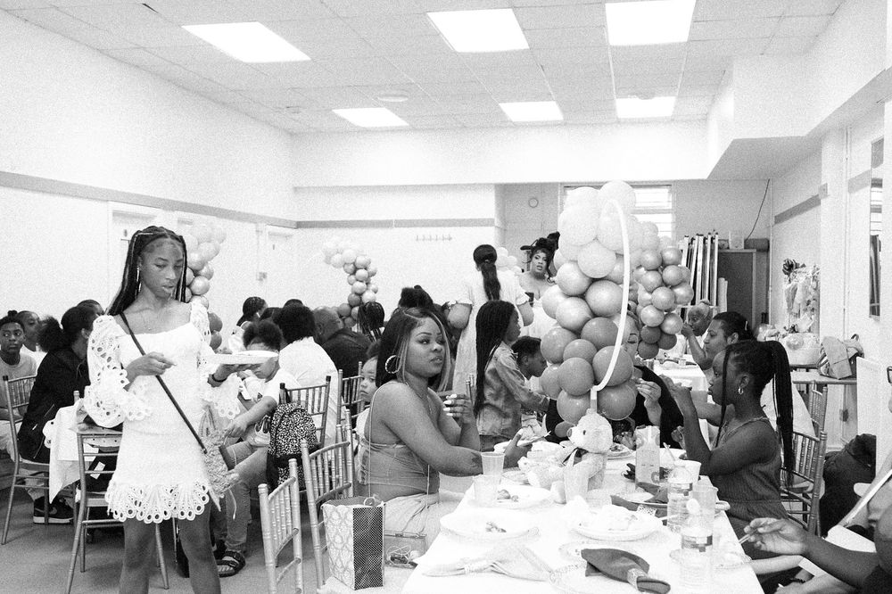 Black and white photo of a baby shower celebration with guests seated at decorated tables.