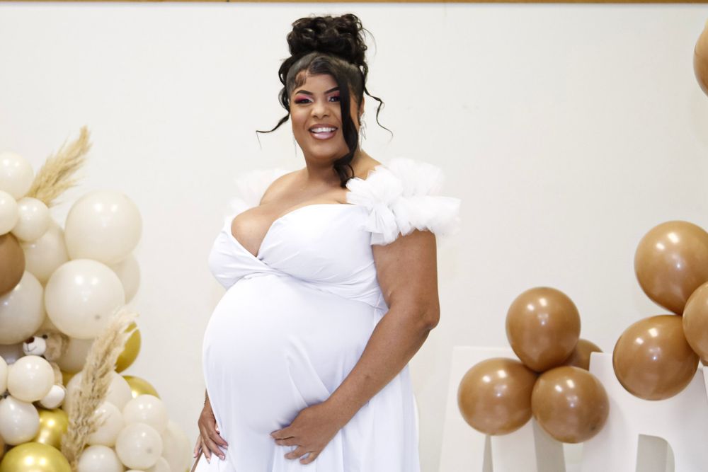 A maternity photo shoot featuring a white off-shoulder gown and gold balloon decorations in the background.
