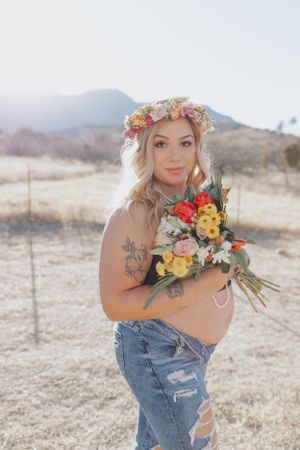 Artistic outdoor photoshoot featuring colorful floral bouquet and denim outfit against mountain backdrop.