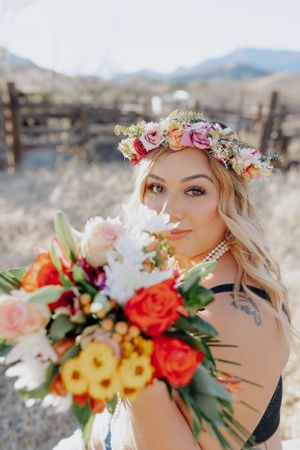 Close-up shot with vibrant flower crown and colorful bouquet against desert mountain scenery.