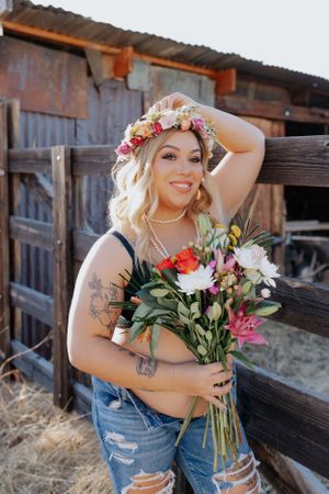 Vintage-style portrait against wooden barn featuring floral arrangements and denim.