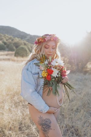 Ethereal outdoor portrait with floral crown and bouquet in warm sunlight.