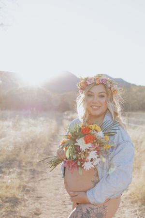 Sun-drenched maternity photo featuring floral crown and colorful bouquet in desert setting.