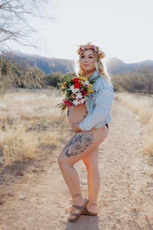 Desert maternity shoot with rustic path, denim jacket and floral accessories.