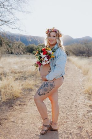 Artistic maternity photography on desert trail with floral crown and bouquet.