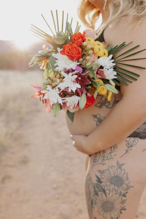 A floral arrangement with white daisies and red roses adorns a sunflower tattoo on bare skin.