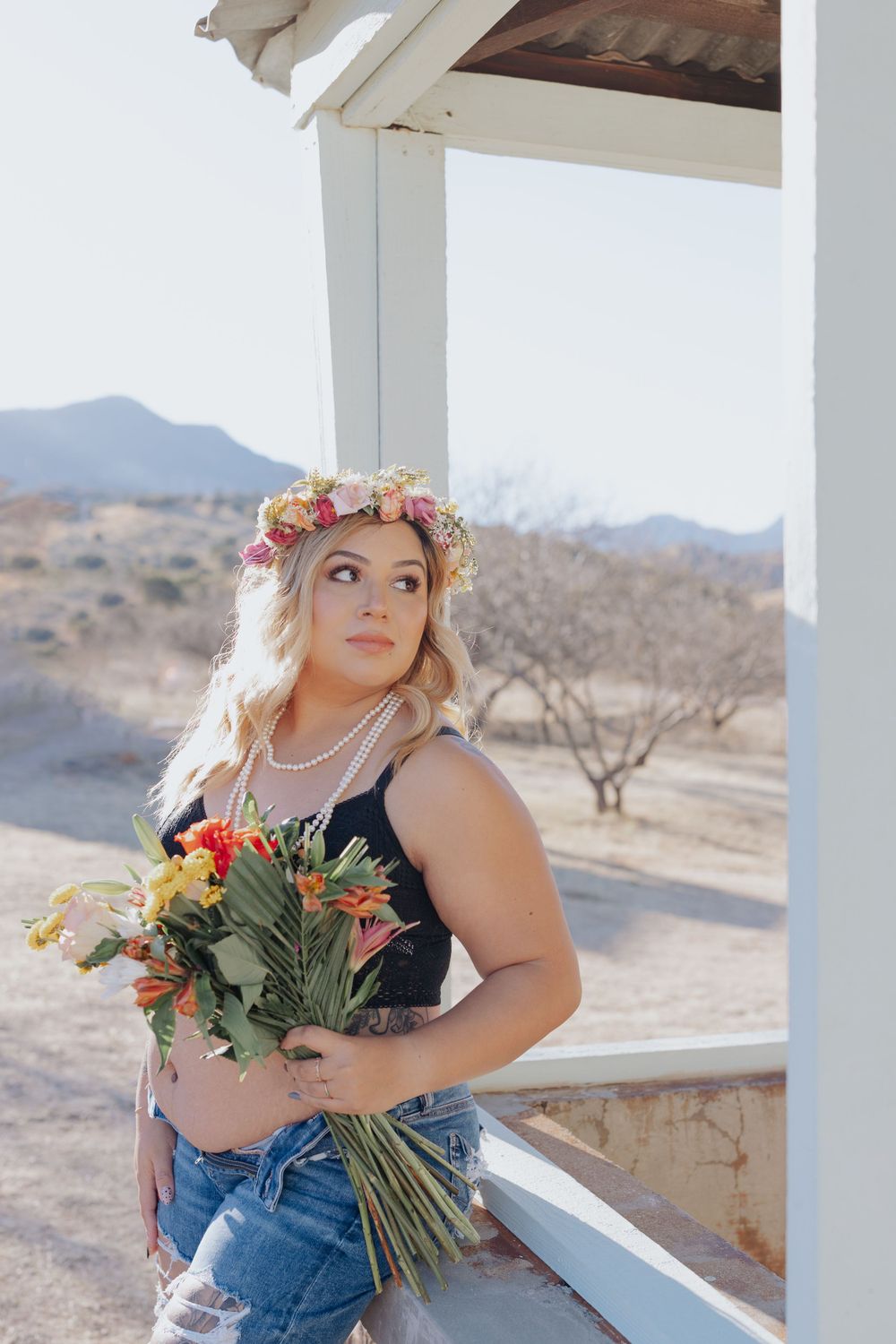 A floral crown adorns someone holding a colorful bouquet while posing under a white pergola.