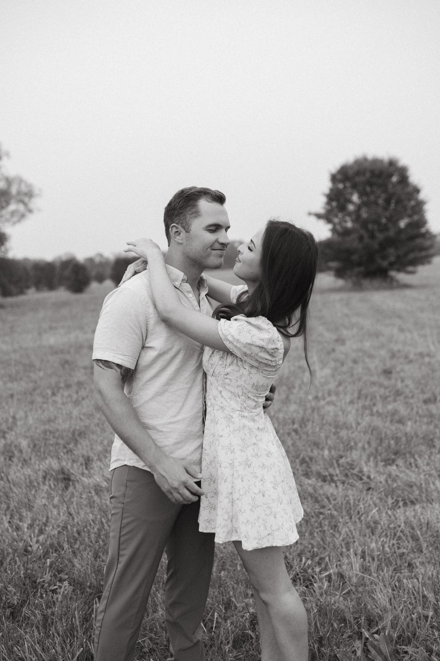A romantic black and white photo of a couple embracing in a field.