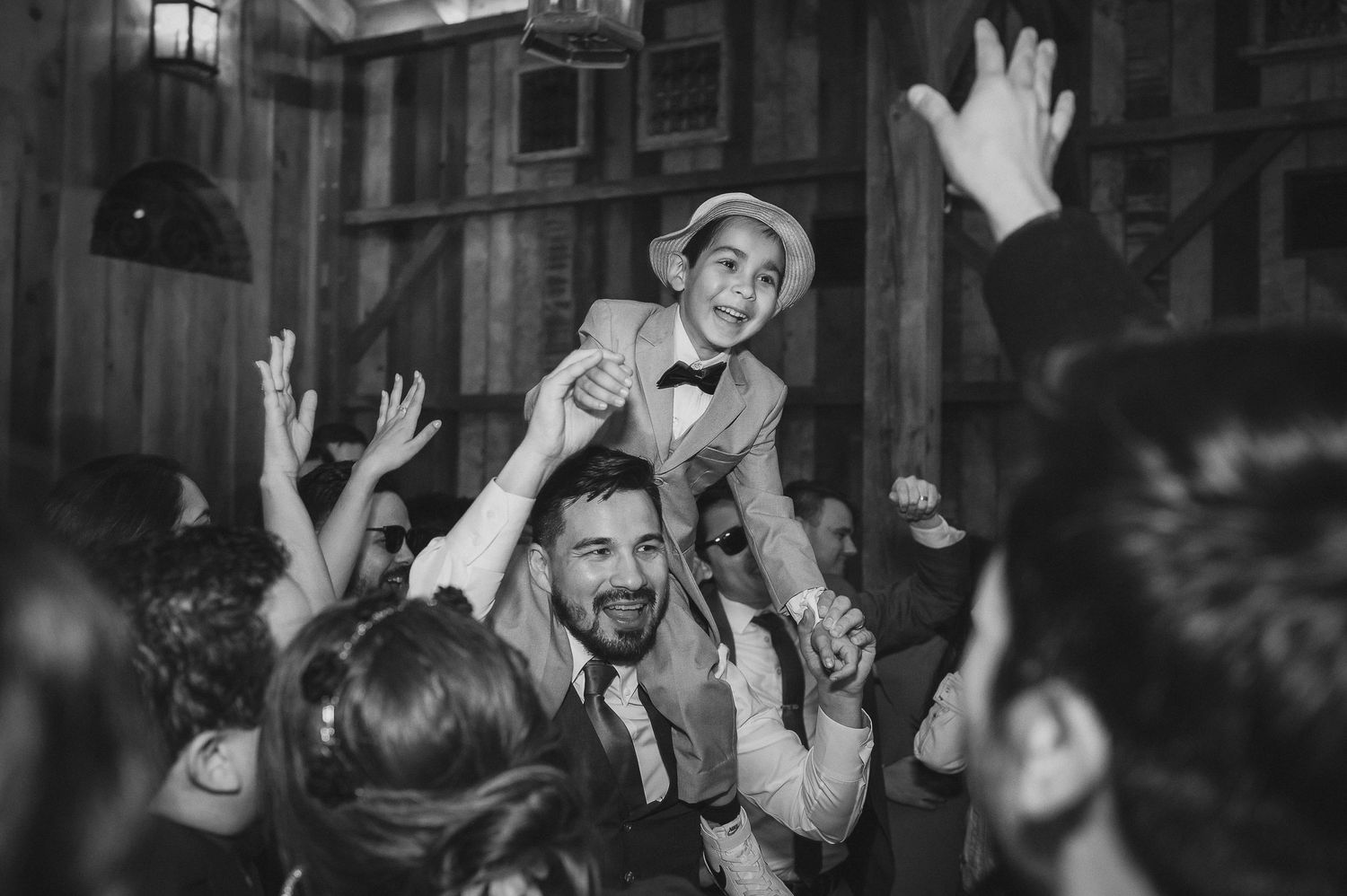 Wedding celebration with joyful dancing and guests lifting someone up during reception party.