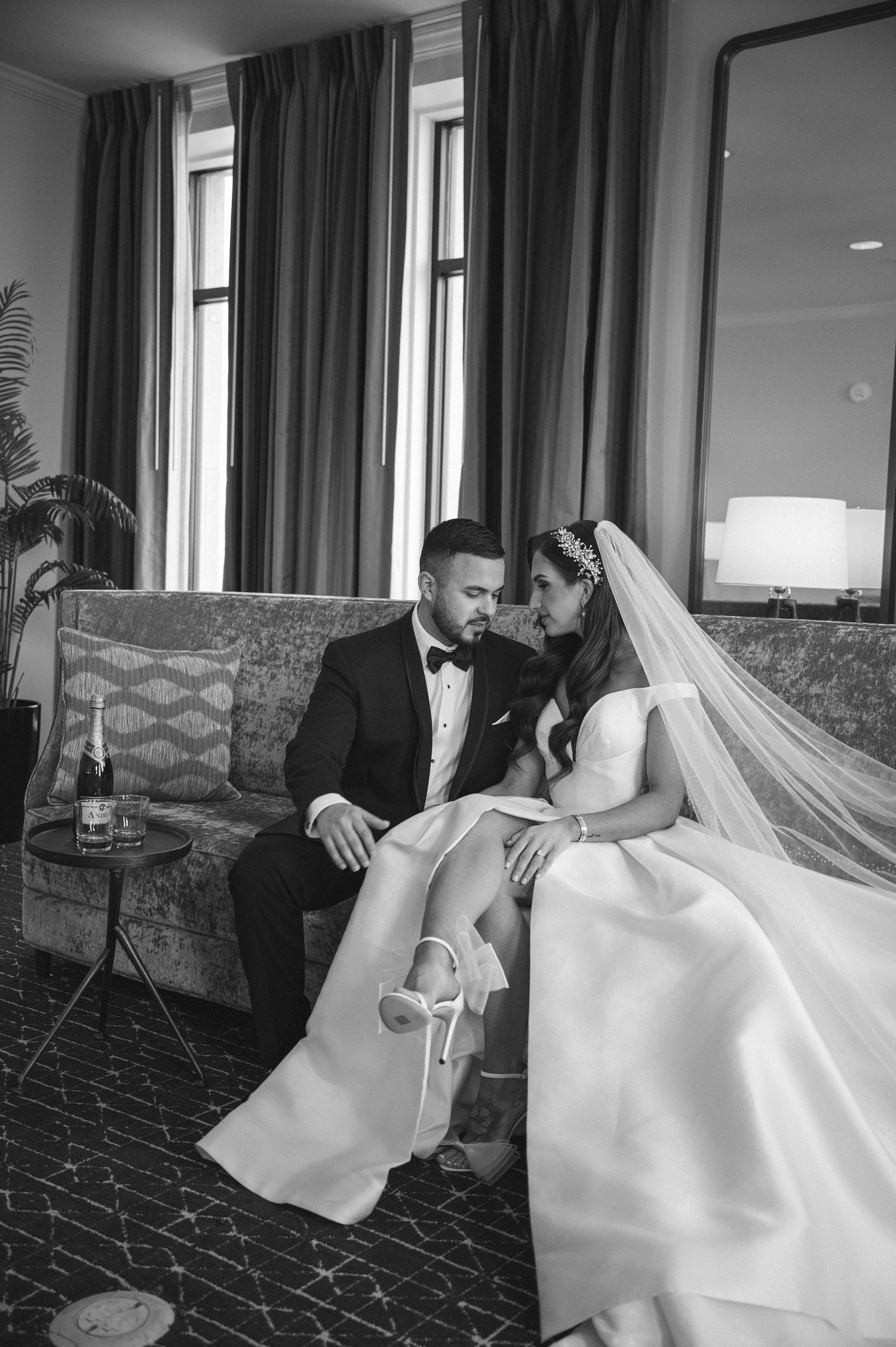 Black and white photo of newlyweds sharing intimate moment on vintage couch.