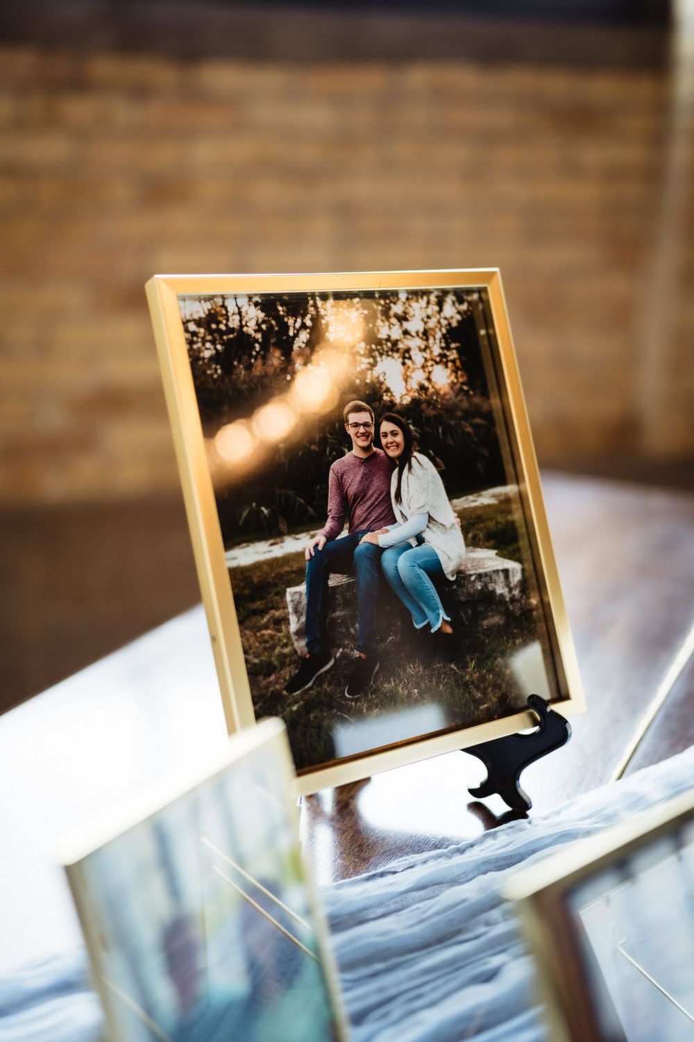 Framed photograph displayed on reflective surface with brick wall background.