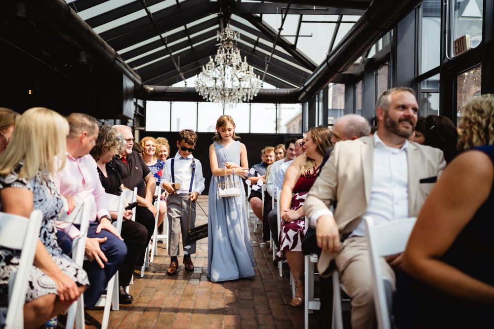 Wedding ceremony processional in industrial venue with wooden floors and crystal chandelier overhead.