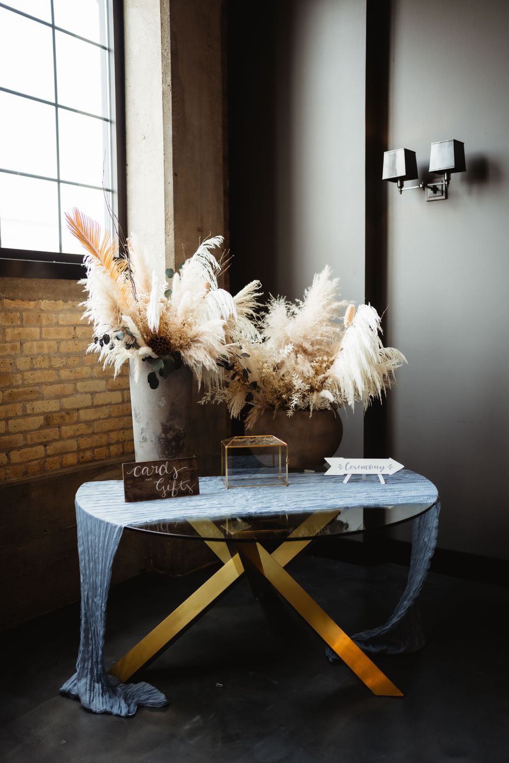 Modern table display with pampas grass arrangements and gold accents against exposed brick wall.