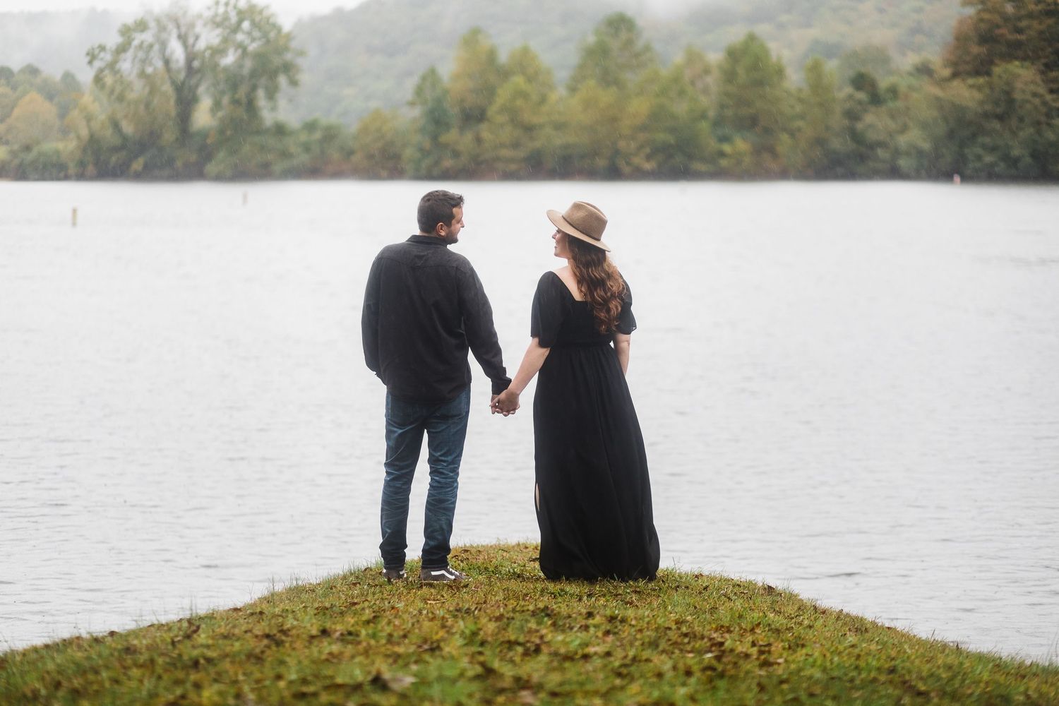 Couple sitting together on grassy hill overlooking serene lake view.