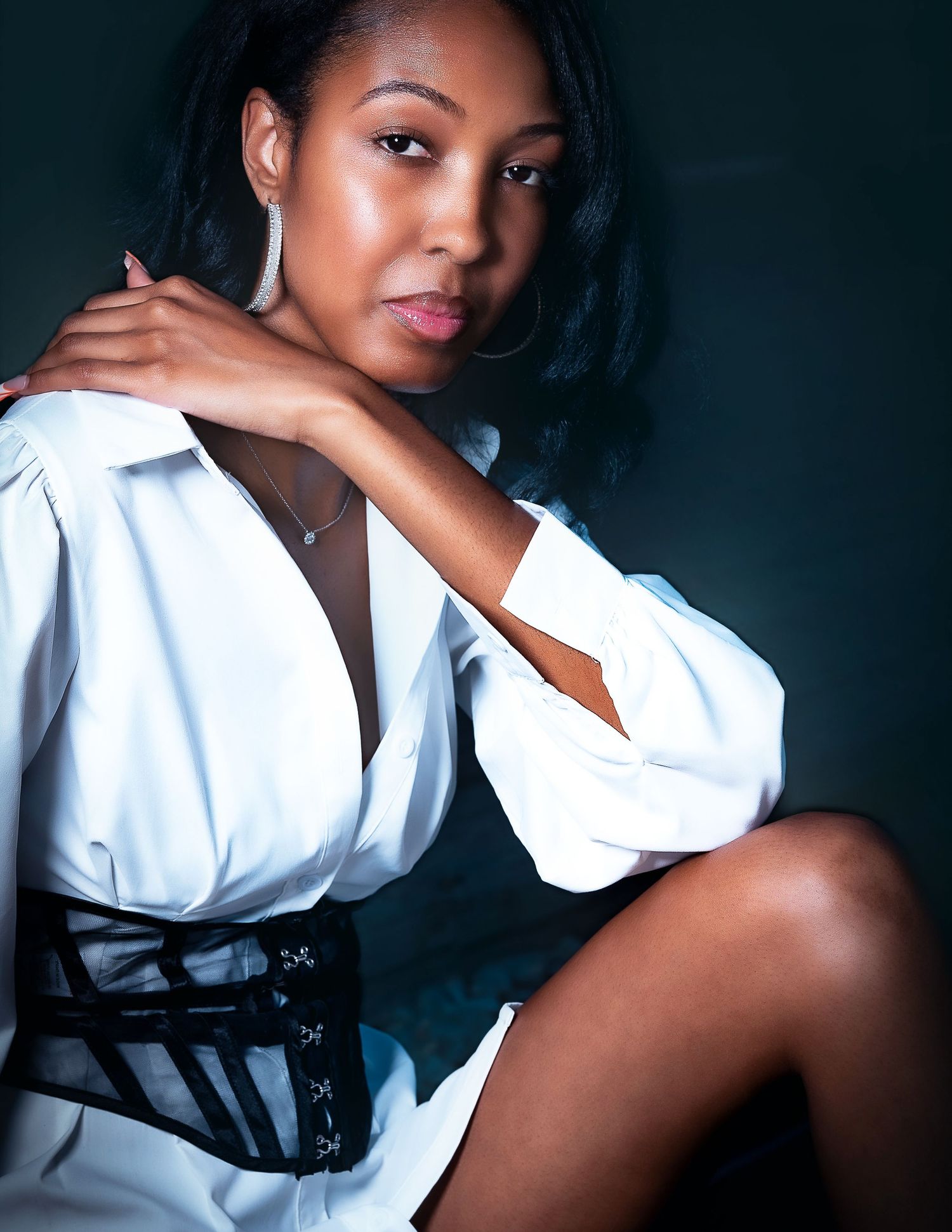 Elegant portrait of model in white shirt with black corset belt against dark background.