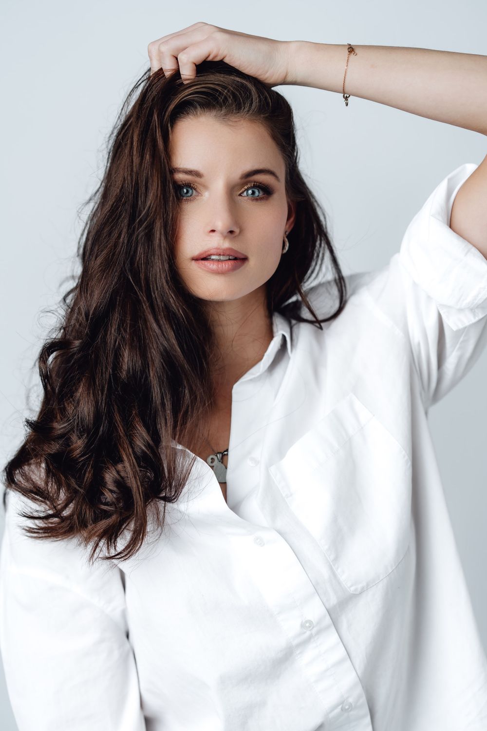 Portrait of woman in white shirt with long dark hair against light background.