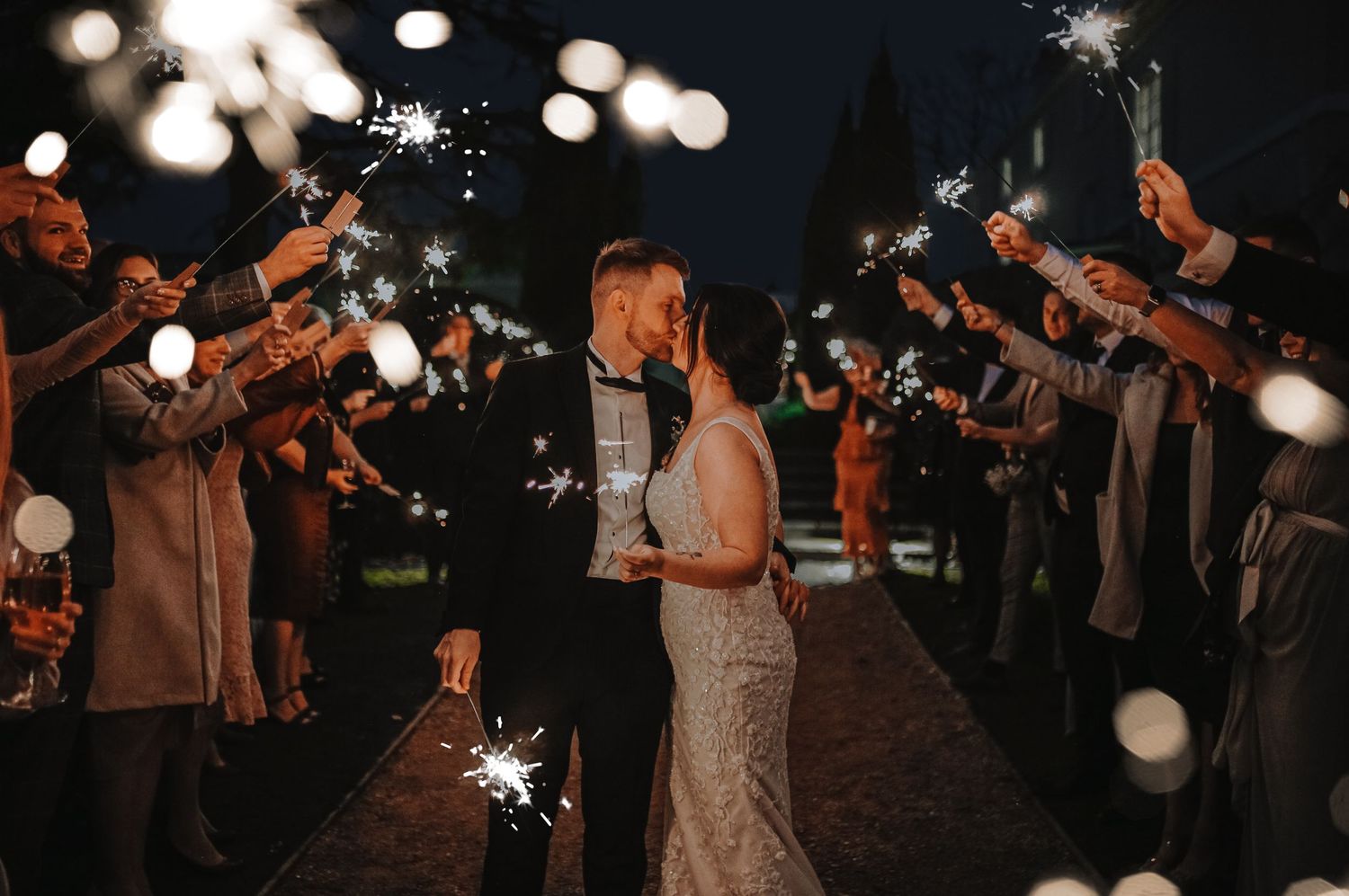 Wedding sparkler exit at night with guests creating magical light tunnel.