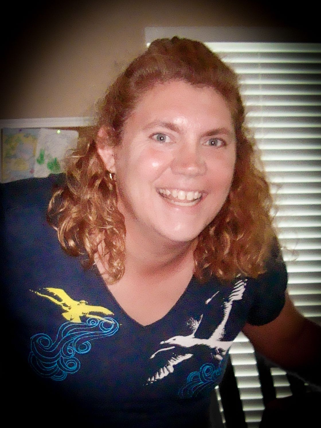 Woman wearing a navy t-shirt with bird designs smiles warmly at the camera.