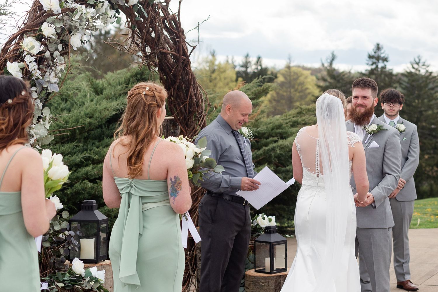 Wedding party gathered under a rustic floral arch during an outdoor ceremony.