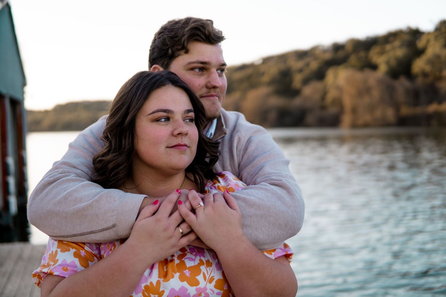 Couple embraces on dock by lake during autumn sunset.