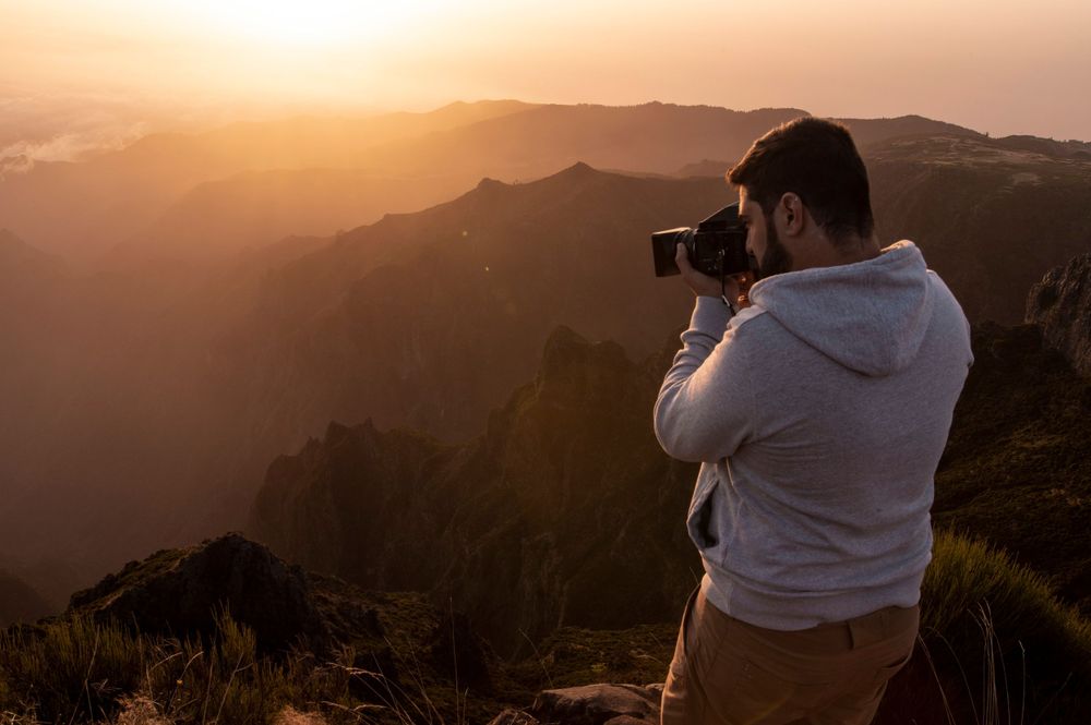 Person taking photos of mountain landscape during golden hour with professional camera.