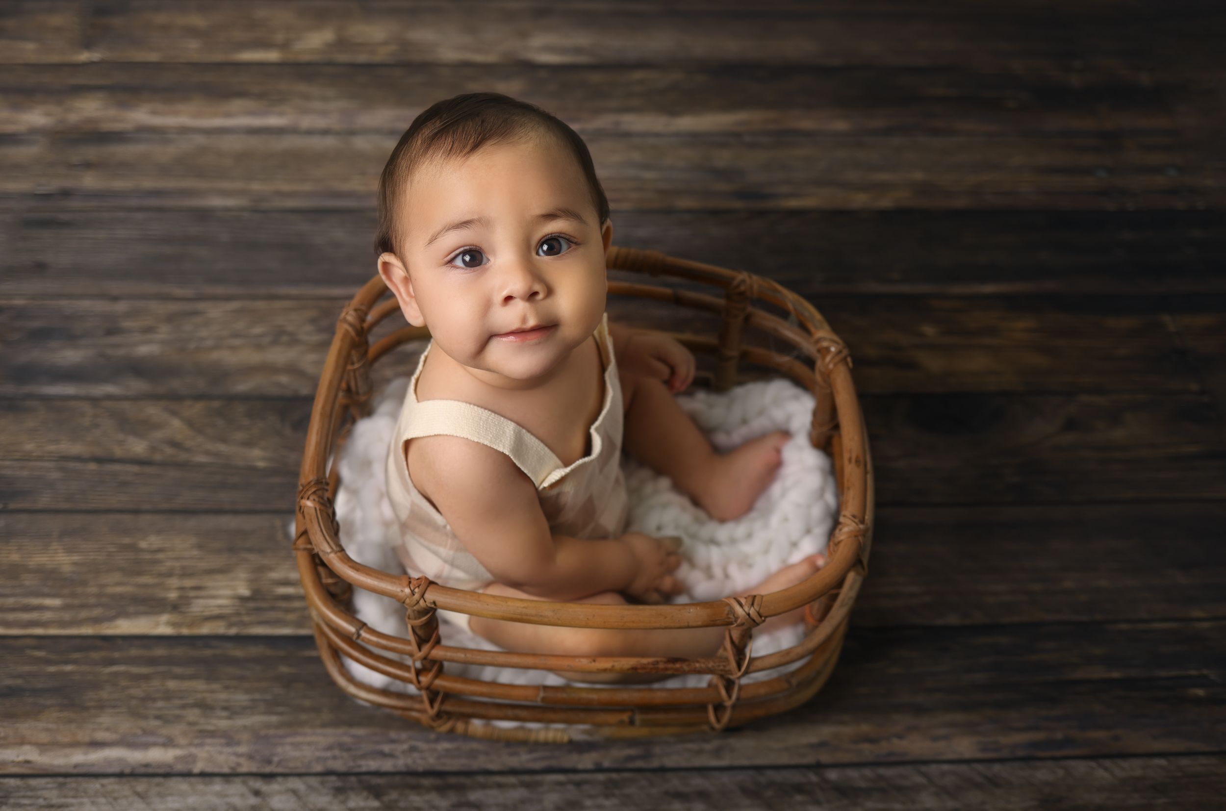 Smiling baby sits in wooden basket during professional photoshoot.