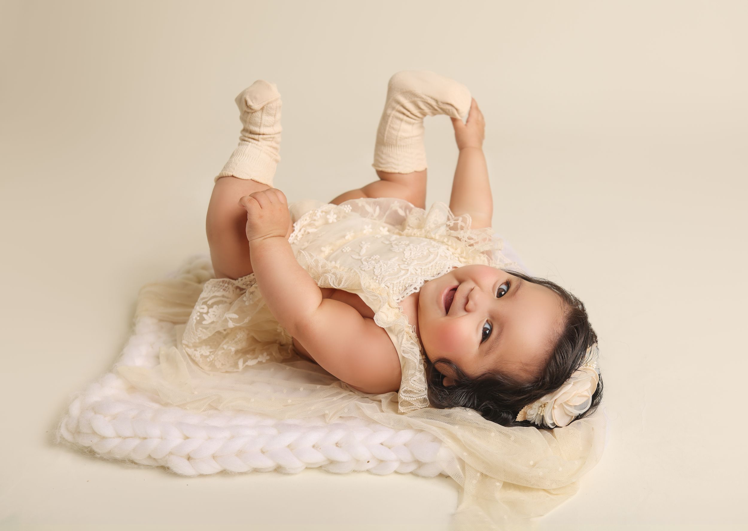 Baby in cream-colored outfit lying on soft blanket during studio photoshoot.