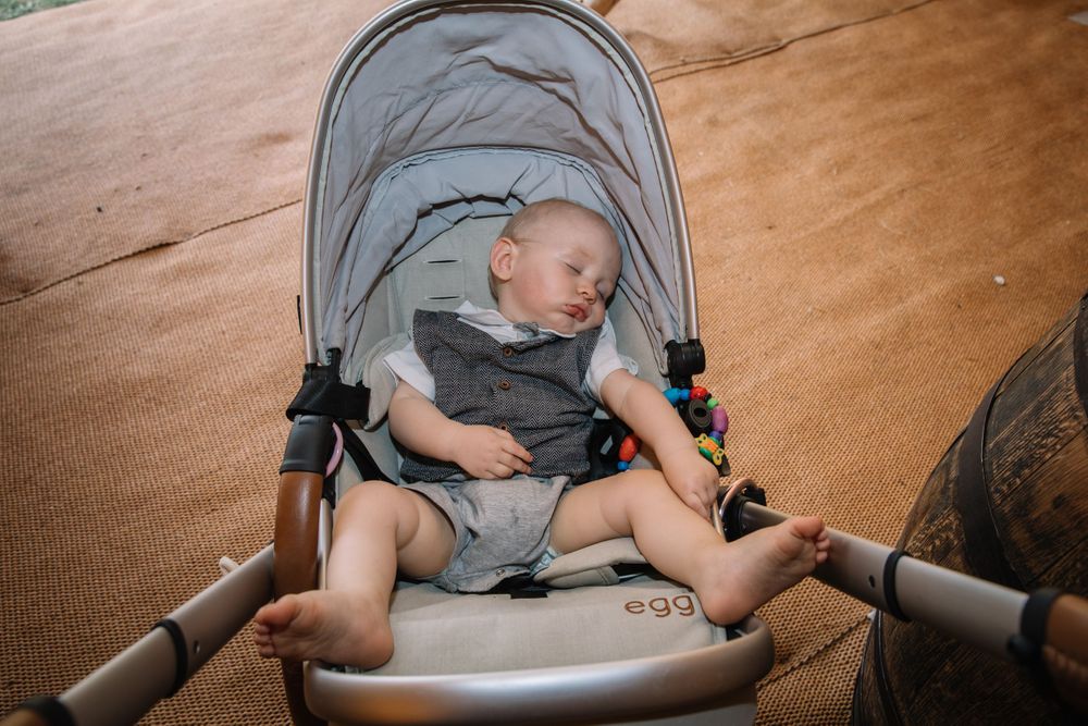 Sleeping baby in grey outfit rests peacefully in stroller at outdoor event.