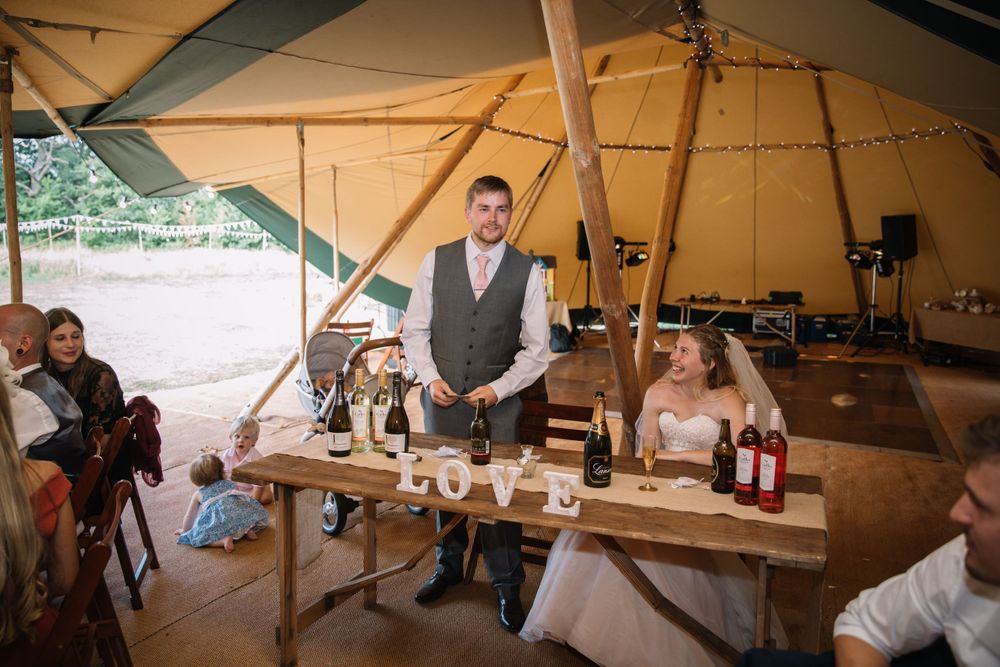 Rustic wedding reception setup inside large canvas tent with wooden tables.