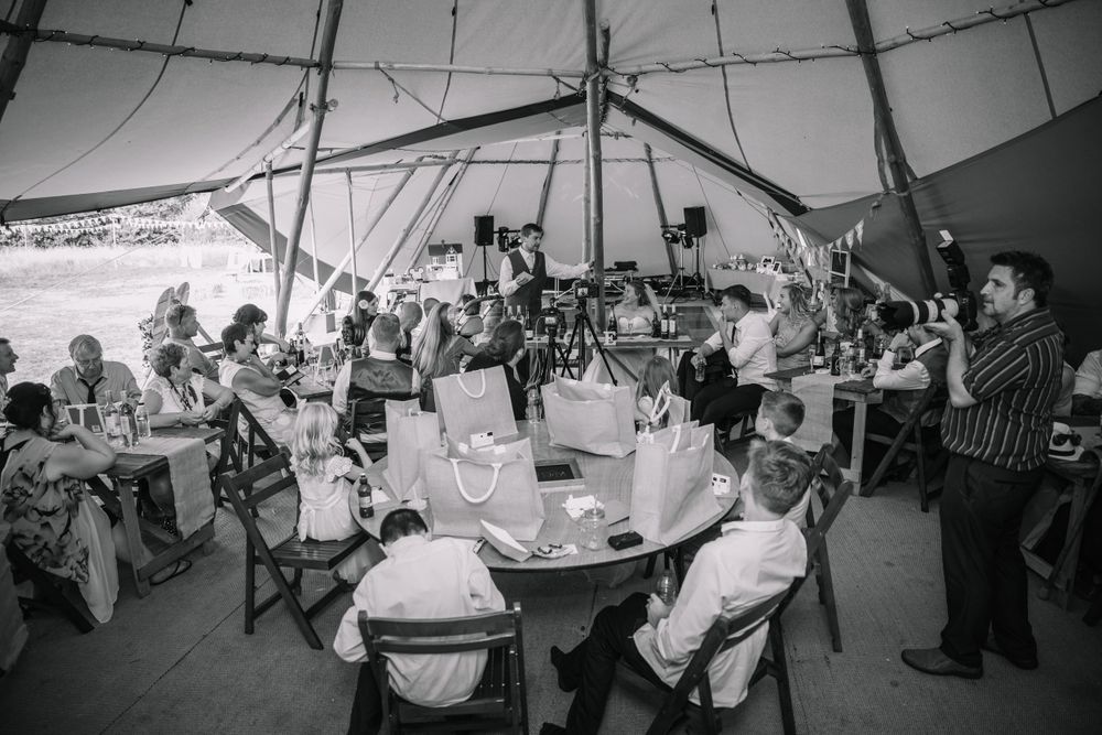 Black and white photo of wedding reception inside large tent with guests at round tables.