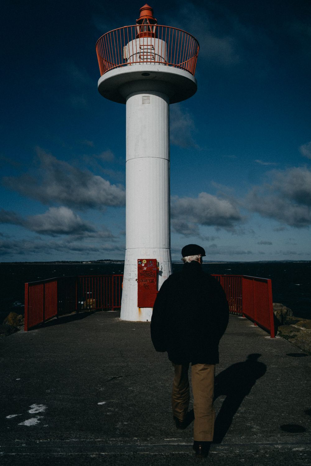 White lighthouse tower with red trim against dark blue sky and clouds.
