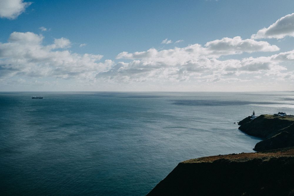Sweeping seascape panorama with bright blue skies and scattered clouds over ocean.