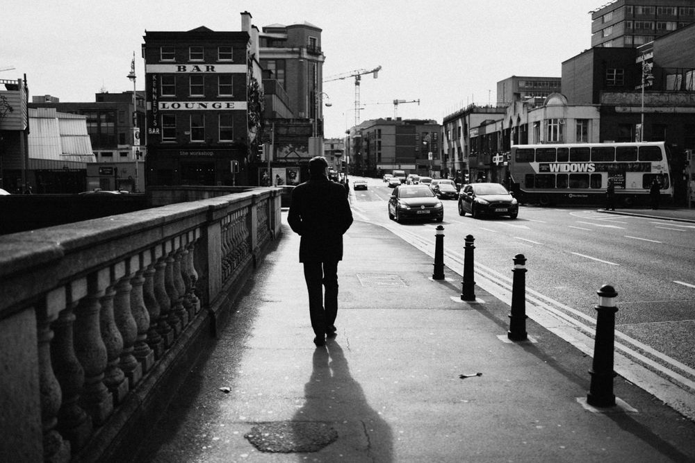 Black and white urban street scene with silhouetted figure walking in rain.