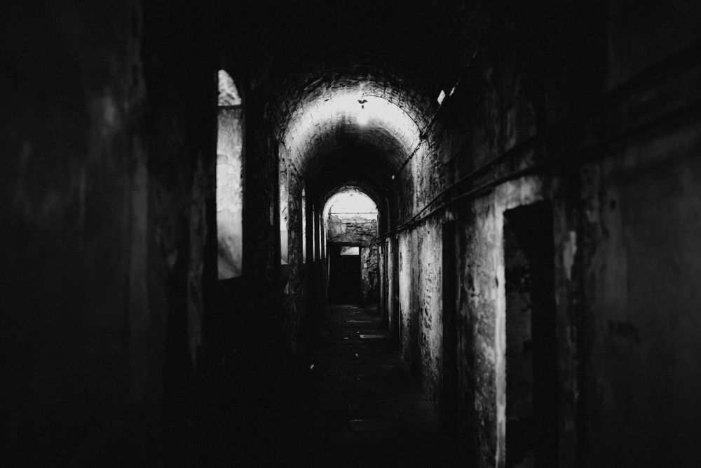 Dark atmospheric corridor with arched stonework and dramatic lighting.
