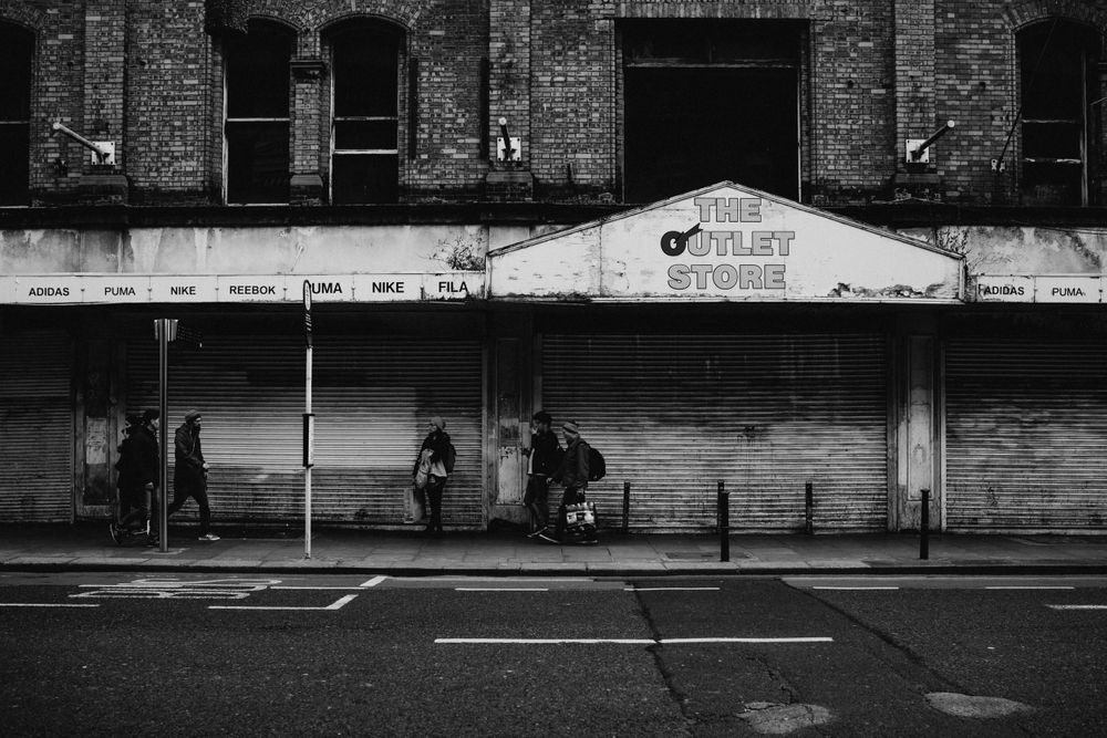 Gritty urban street scene with brick buildings and storefronts in black and white.